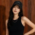 Woman wearing a black cap and black tank top against a wooden background