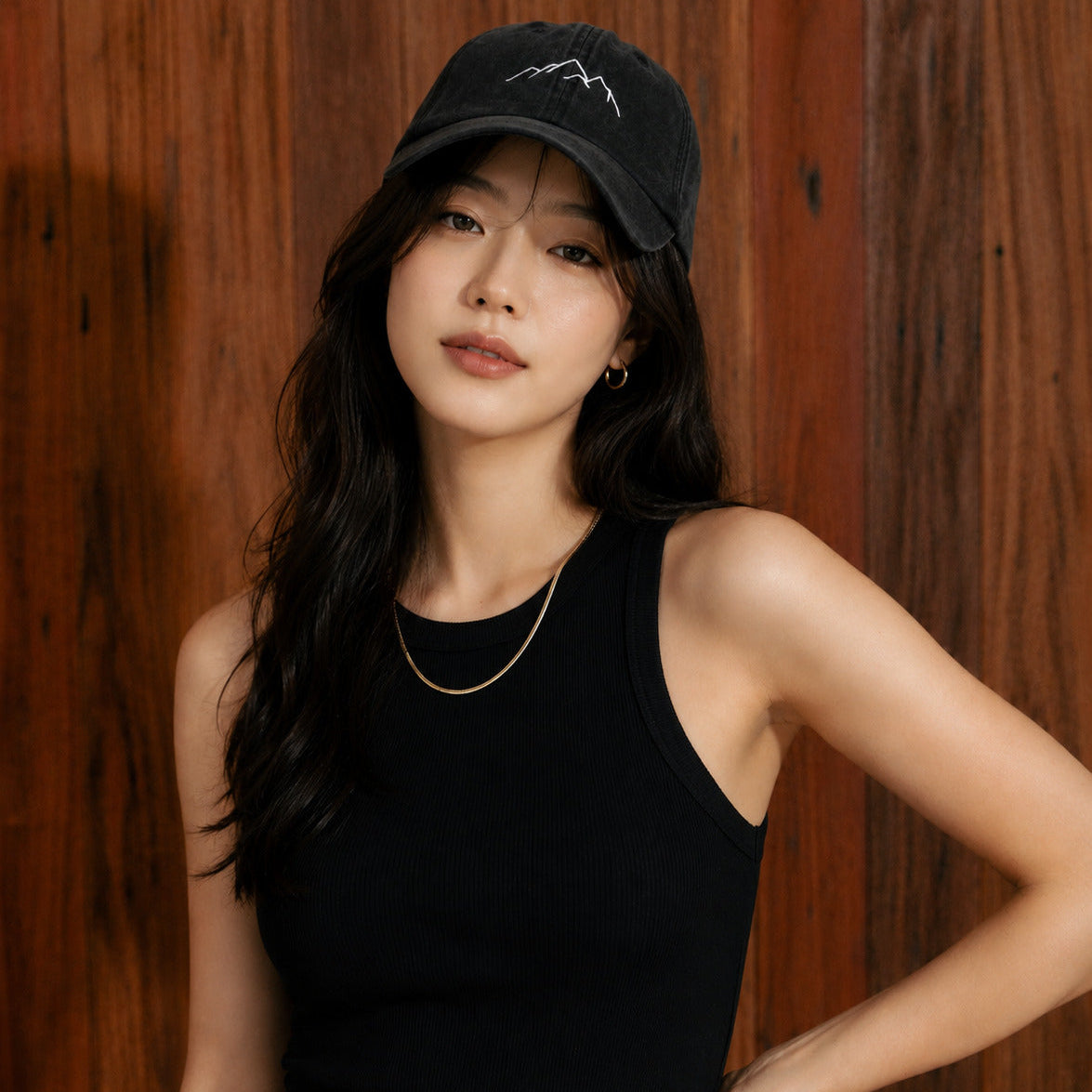 Woman wearing a black cap and black tank top against a wooden background