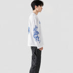 Person wearing a white shirt with blue dragon design and dark pants on a white background