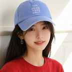 Woman wearing a blue cap with 'The Good Vibes Only' text and a red shirt.