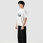 Person wearing a white t-shirt with a graphic design and black pants on a light gray background