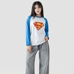 Person wearing a Superman-themed shirt with blue sleeves and gray pants on a white background