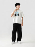 Person wearing a white t-shirt with a graphic design and black pants on a light gray background