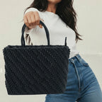 Person holding a black woven handbag against a neutral background