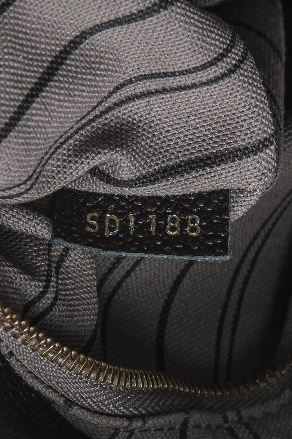 A close-up of the gold-tone logo key bell hanging from the strap