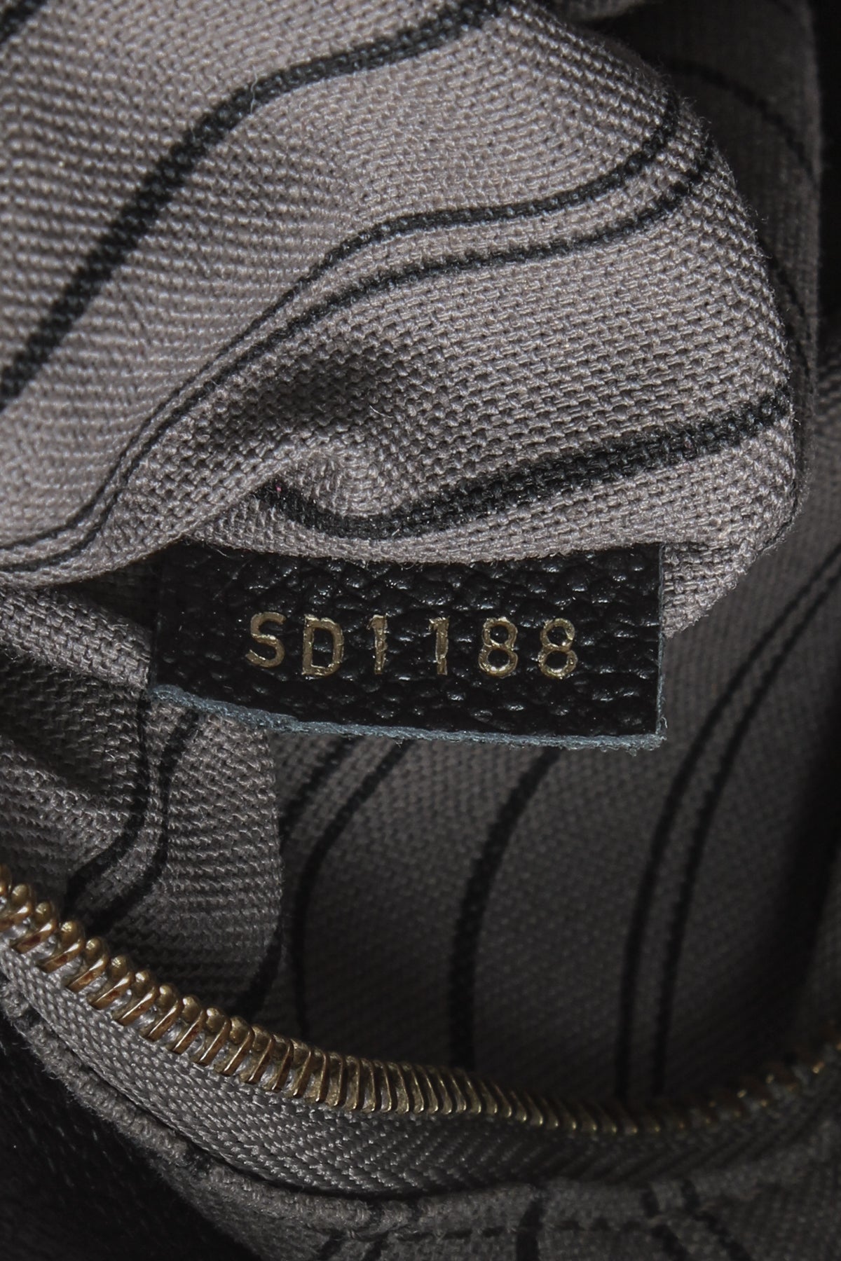 A close-up of the gold-tone logo key bell hanging from the strap